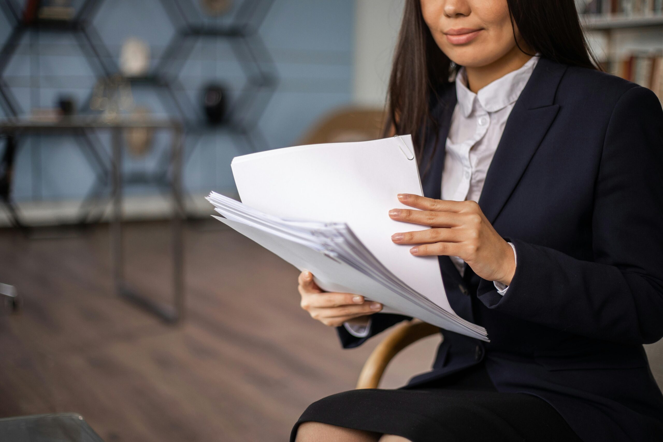A professional woman in a suit reviewing documents while seated in an elegant office setting.